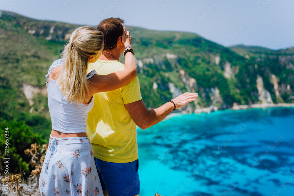 Petani view point young woman closing her boyfriend eyes in front of gorgeous seascape panorama. Turquoise Petani beach on Kefalonia island Greece Petani view point young woman closing her boyfriend eyes in front of gorgeous seascape panorama. Turquoise Petani beach on Kefalonia island Greece