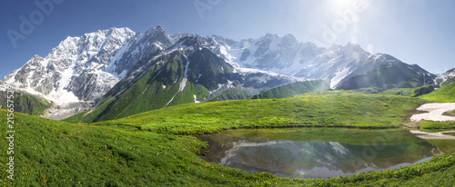 Mountain landscape of Svaneti on bright summer sunny day. Mountain lake, hills covered green grass on snowy rocky mountains background. Caucasus peaks in Georgia. Amazing view on wild georgian nature. photo