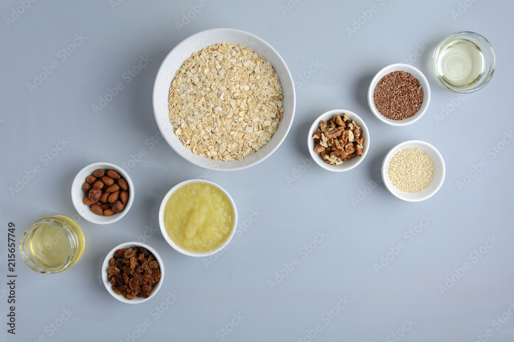 Ingredients for cooking homemade granola: oatmeal, applesauce, honey, oil, almond, walnut, raisin, flax and sesame seeds on wooden gray background. Flat lay. Top view.