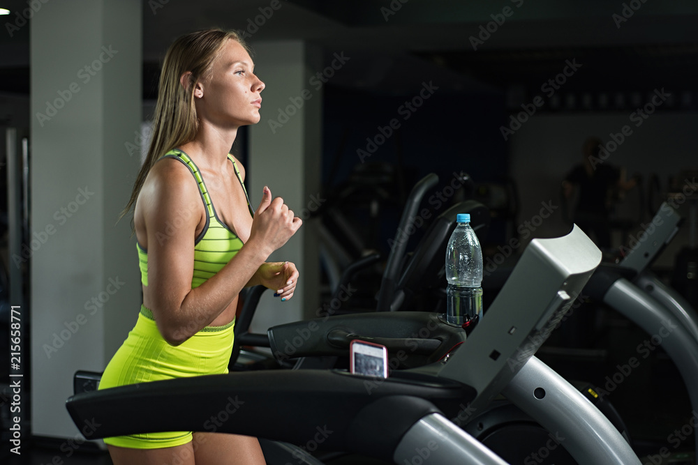 Beautiful girl running on treadmill in gym, healthy lifestyle concept