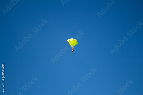 Man, a paratrooper is flying through the blue sky amidst white clouds on a parachute