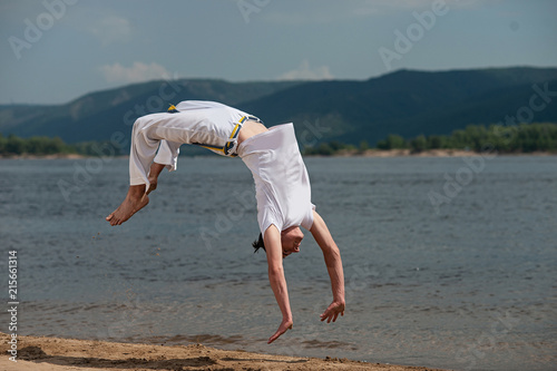 Acrobat performs an acrobatic trick, somersault on the beach.