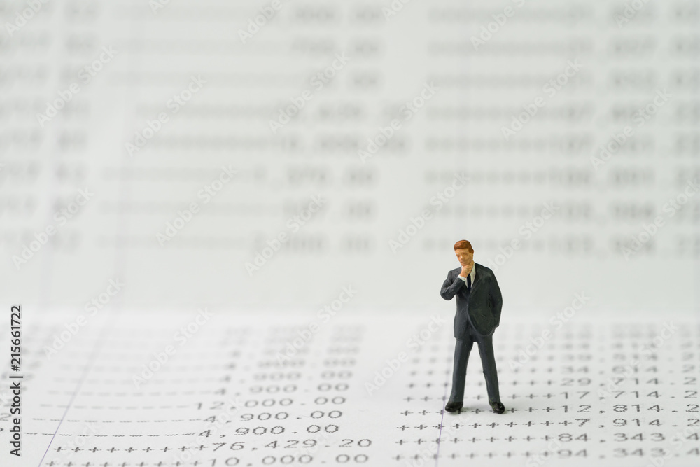 Saving or deposit account, compound interest or banking concept, miniature businessman standing and thinking on numbers of money printed on paper bank account book Saving or deposit account, compound interest or banking concept, miniature businessman standing and thinking on numbers of money printed on paper bank account book
