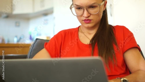 Portrait of a woman in red working behind a laptop monitor. Meiling, woman freelancer, secretary, office employee, manager. Girl wearing optical glasses photo