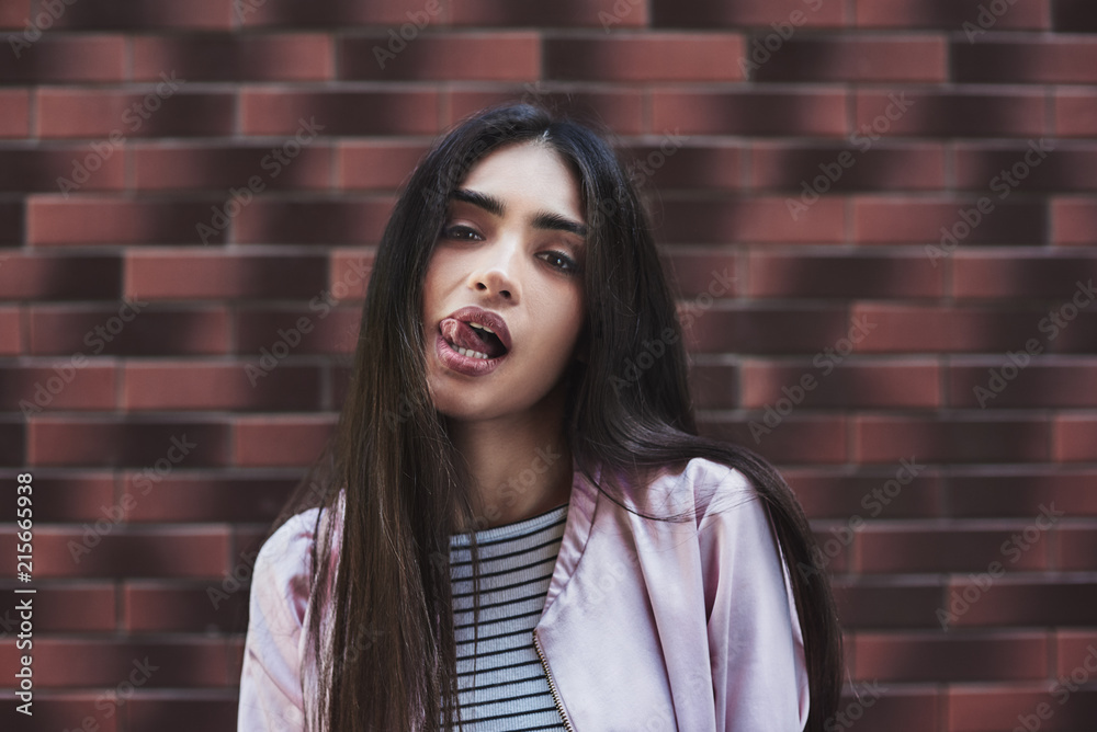 Young woman in pink jacket stading isolated on wall tongue out l Young woman in pink jacket stading isolated on wall tongue out l