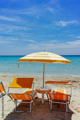 Fototapeta Naklejka Na Ścianę i Meble -  Beach equipment, chairs and sun umbrella on white sandy beach with light blue sea water, beach vacation concept