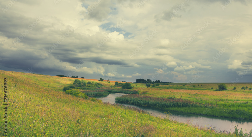 Cloudy summer landscape with fields,meadows,woods and small river.Dark stormy clouds in dramatic overcast sky.Rainy season.Traveling through the plains of Tula region,Russia. Cloudy summer landscape with fields,meadows,woods and small river.Dark stormy clouds in dramatic overcast sky.Rainy season.Traveling through the plains of Tula region,Russia.