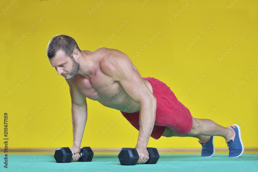 Strong attractive man performs exercises using a resistance band. Photo of muscular male isolated on yellow background. Strength and motivation