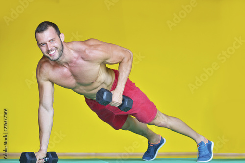 Strong attractive man performs exercises using a resistance band. Photo of muscular male isolated on yellow background. Strength and motivation