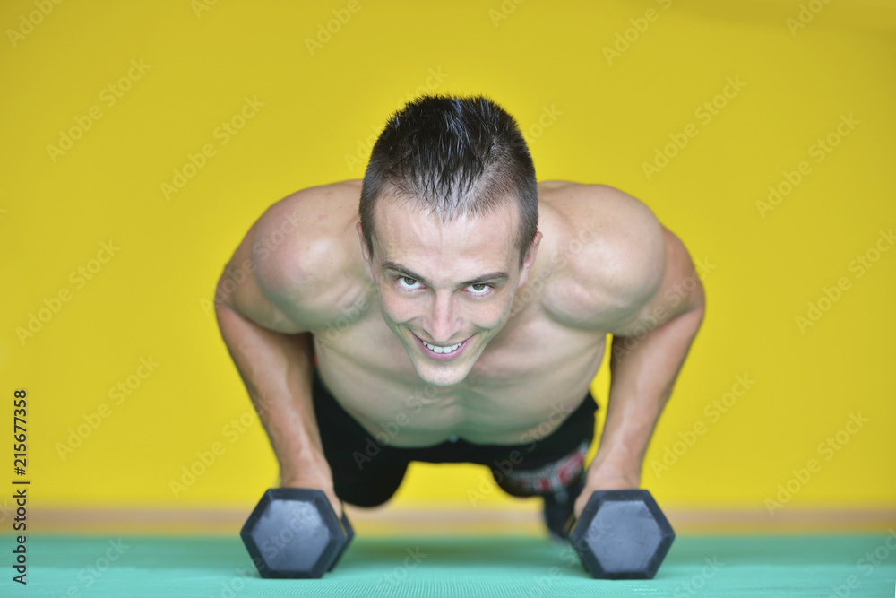 Strong attractive man performs exercises using a resistance band. Photo of muscular male isolated on yellow background. Strength and motivation Strong attractive man performs exercises using a resistance band. Photo of muscular male isolated on yellow background. Strength and motivation