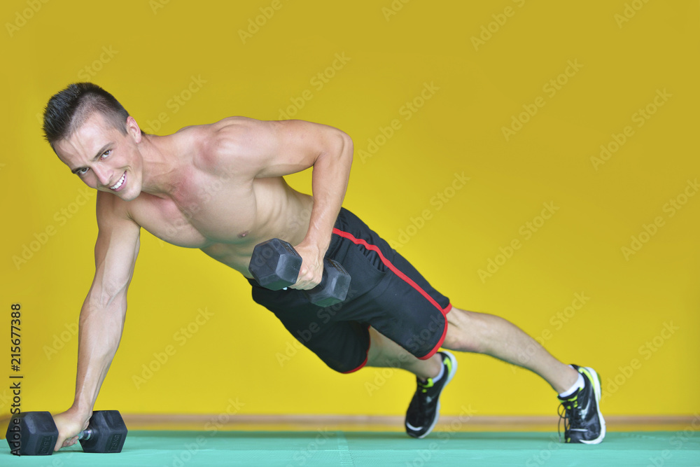 Strong attractive man performs exercises using a resistance band. Photo of muscular male isolated on yellow background. Strength and motivation Strong attractive man performs exercises using a resistance band. Photo of muscular male isolated on yellow background. Strength and motivation