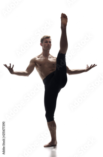 front view, one young man, ballet dancer, standing on one leg, other leg in high in mid-air, white background. arms outstretched.