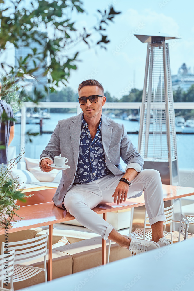 custom made wallpaper toronto digitalConfident successful man with stylish hair dressed in modern elegant clothes holds cup of coffee while sitting on a table at outdoor cafe against the background of city wharf.
