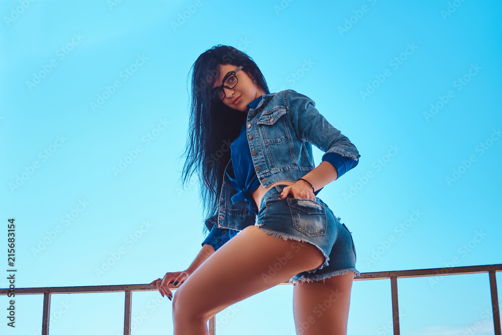 Seductive sexy brunette girl wearing short shorts and jeans jacket posing  while sitting on guardrail against a sky background. Stock Photo | Adobe  Stock