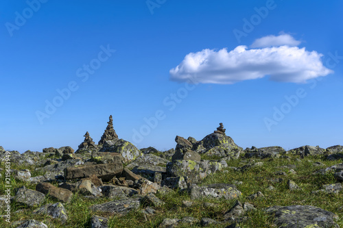 bright landscape of a high-altitude plateau with folded travelers pyramids cairns of stones under a blue sky with clouds..