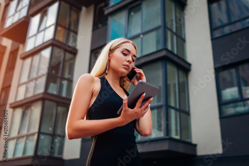 Young blonde businesswoman using smartphone by contemporary business center in city. Communiation