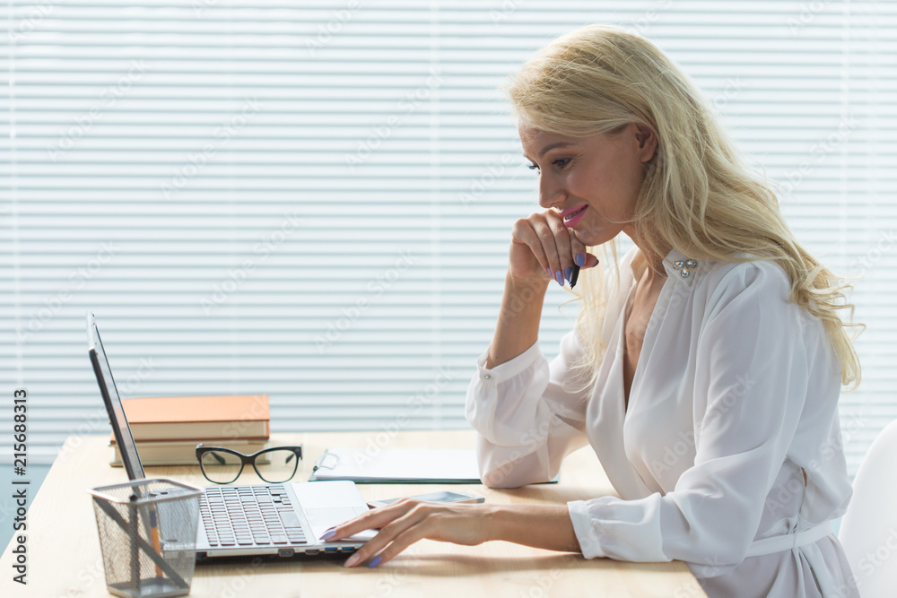 Working, business, technology and people concept - young woman working in office wuth laptop and writing notes Working, business, technology and people concept - young woman working in office wuth laptop and writing notes
