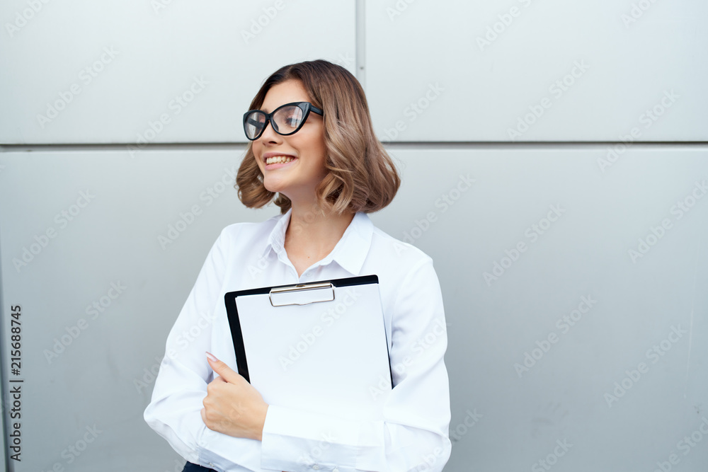 business woman with glasses smiling holding documents against a building street business woman with glasses smiling holding documents against a building street