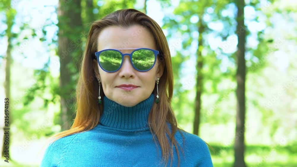 Portrait of a young woman in sunglasses with mirror glasses. She is wearing a blue turtleneck with a high collar. In the background a blurred forest. Portrait of a young woman in sunglasses with mirror glasses. She is wearing a blue turtleneck with a high collar. In the background a blurred forest.