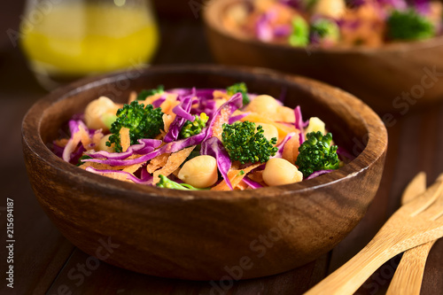Frischer Salat aus Rotkohl, Kichererbsen, Karotten und Broccoli serviert in Holzschüsseln, fotografiert mit natürlichem Licht (Selektiver Fokus, Fokus in die Mitte des Bildes)