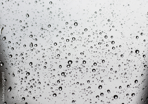 Pure raindrops on a window glass surface on a gray clouds background. Water drops pattern close up shot