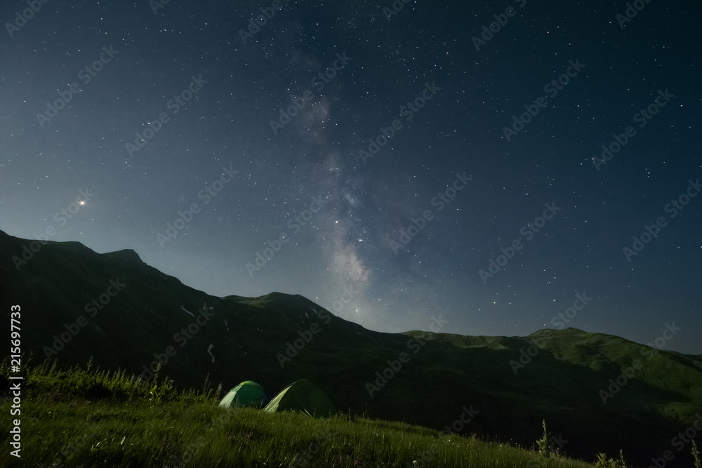 Night landscape of two camping tents and a mountain range at the background.
