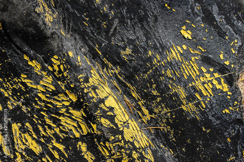 Abstract black burnt rubber background with yellow peeling paints. Dirty scratched burn elastic gum with orange dye peels photo