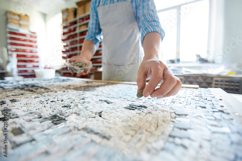 Close up shot of unrecognizable artist laying out tiles while creating mosaic in workshop, copy space