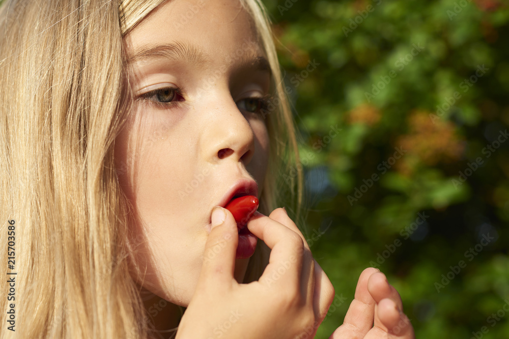 Child cute girl holding fresh chilli pepper and preparing to eat it outside in summer garden. Greenery background