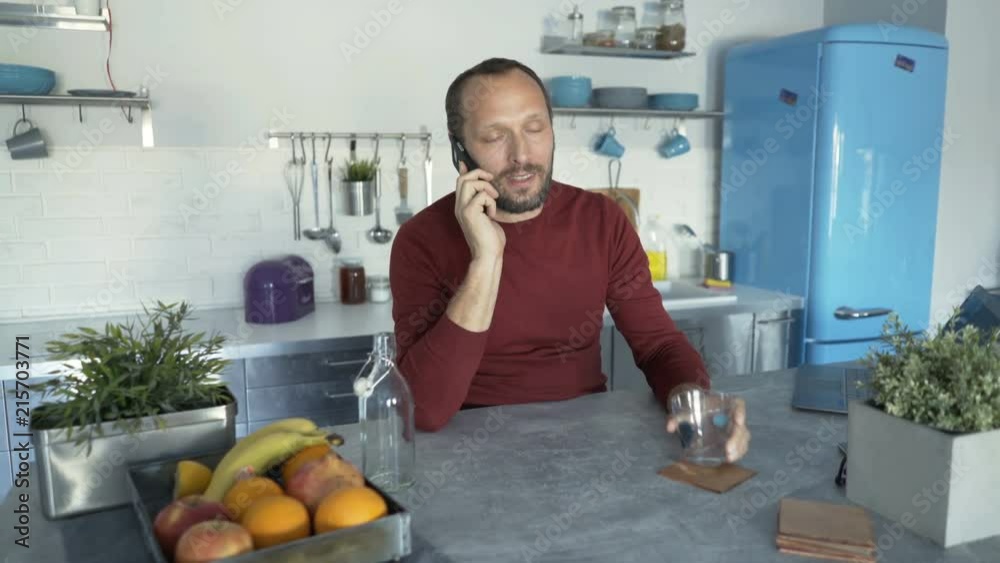 Handsome man talking on cellphone in the kitchen and drinking water, steadycam shot
Handsome man talking on cellphone in the kitchen and drinking water, steadycam shot