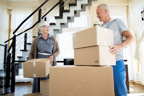 Portrait of happy senior couple packing cardboard boxes while moving to new house