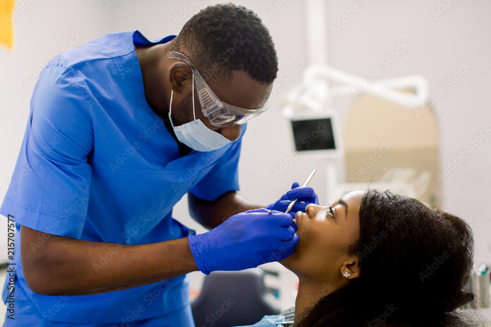 Male african dentist examining a patient with tools in dental clinic