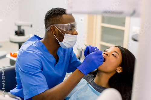 Male african dentist examining a patient with tools in dental clinic. African female patient getting dental treatment in dental clinic photo