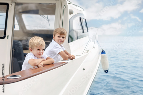 Two cute caucasian blond boys on board of white luxury yacht on bright summer day. Siblings having fun learning yachting tohether. Travel and adventure with children concept © Kirill Gorlov