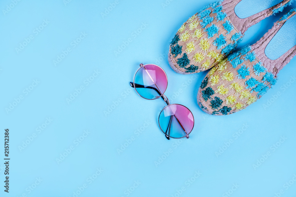 Summer fashion flatlay with gradient round sunglasses and espadrille sandals on the blue background. Perfect beach set for holidays on the sea. Marina style.