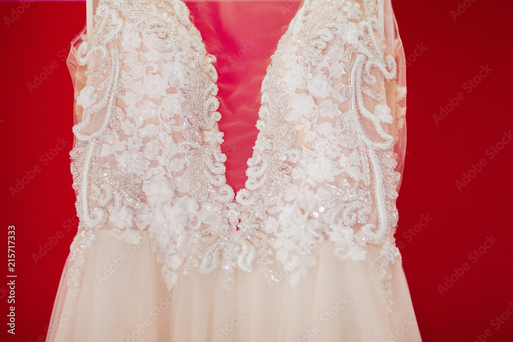 Cream wedding dress close-up, lace and beads. Red background