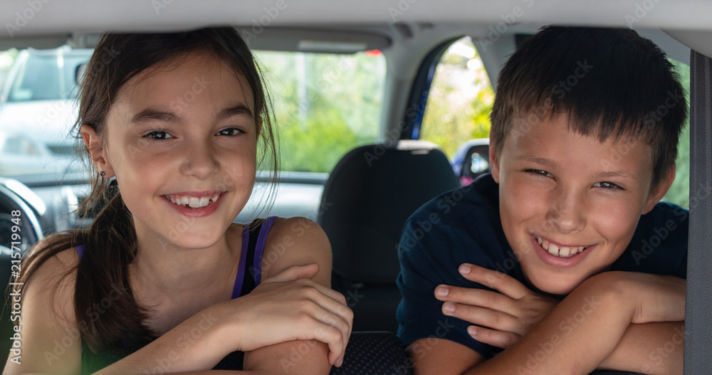 background. friends. beautiful children, (guy and girl) are sitting in the car, in the back seat and smiling
