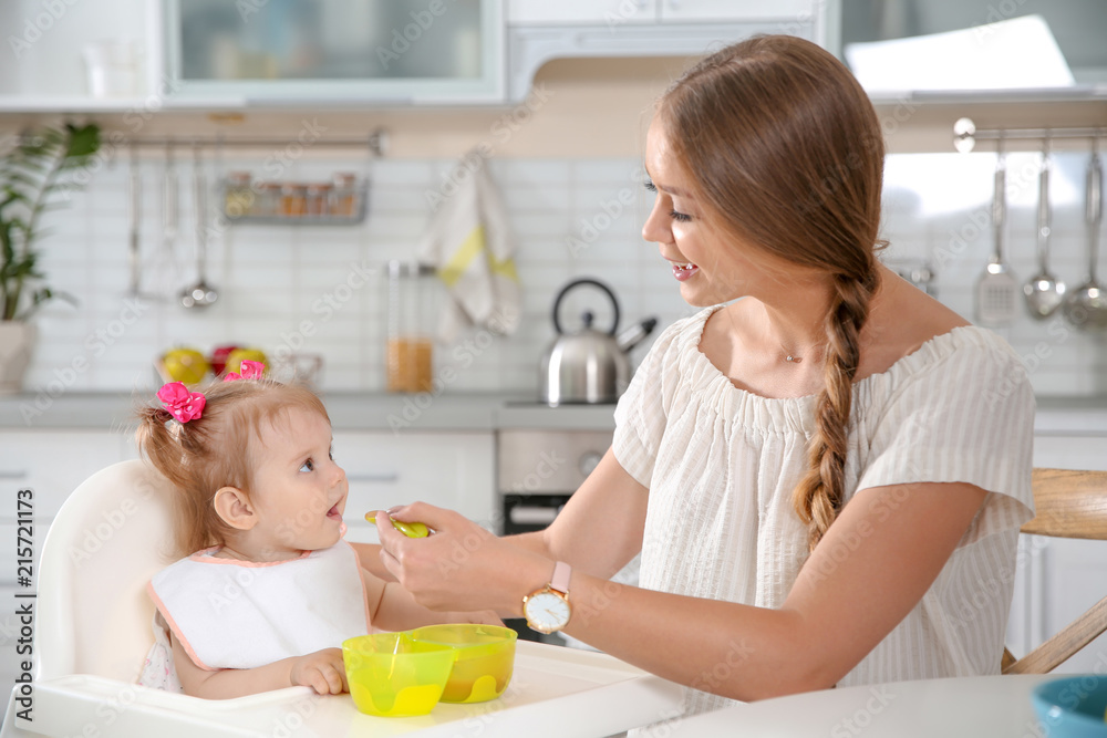 Mother feeding her little baby with healthy food in kitchen Mother feeding her little baby with healthy food in kitchen