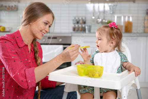 Mother feeding her little baby with healthy food in kitchen