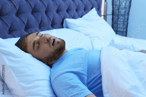 Young man snoring while sleeping in bed at night. Sleep disorder photo