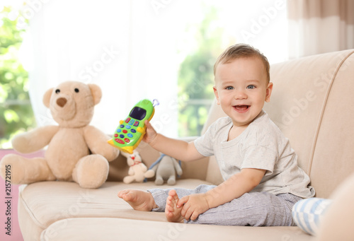 Adorable little baby with toy phone on sofa at home photo
