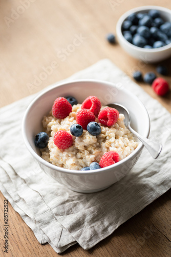 Bowl of oatmeal porridge with berries on textile on wooden table. Selective focus. Healthy breakfast, healthy eating concept