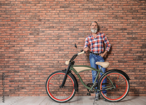 Portrait of handsome mature man with bicycle near brick wall