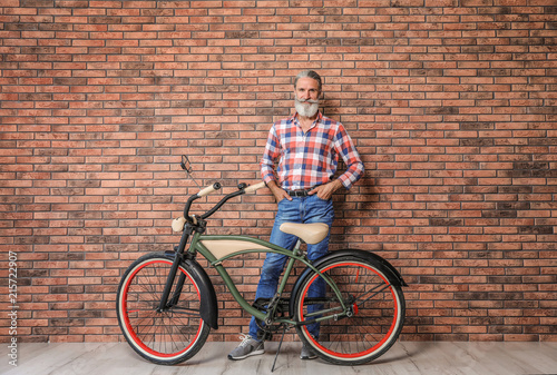 Portrait of handsome mature man with bicycle near brick wall