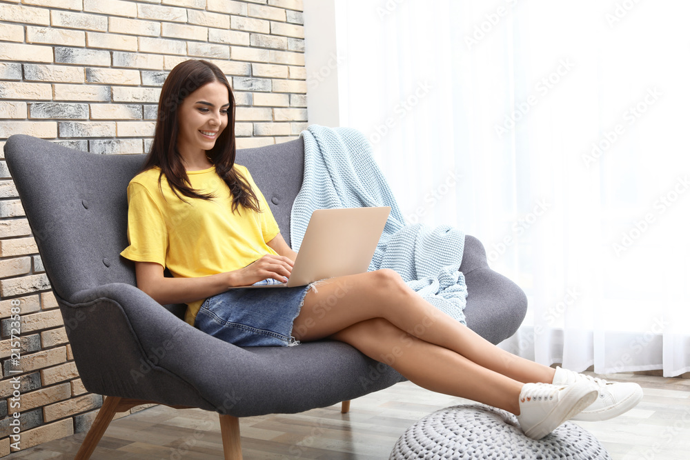 Young woman with modern laptop sitting on sofa at home Young woman with modern laptop sitting on sofa at home