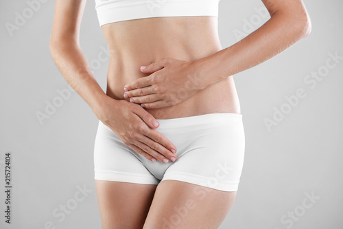 Young woman holding hands near panties on grey background. Gynecology concept