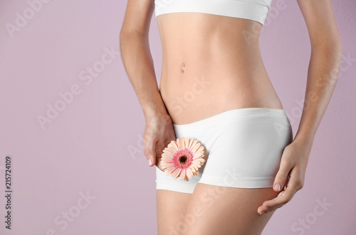 Young woman with gerbera flower on color background. Gynecology concept photo