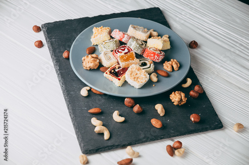 Traditional oriental sweets and nuts: hazelnuts, cashews on a white wooden background. Turkish dessert is the locus of Rahat. View from above. Place under the text. photo