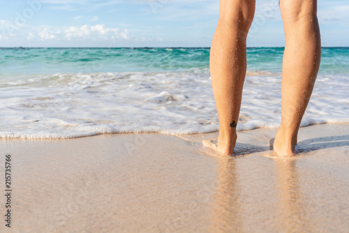 Young woman legs and feet standing on beach