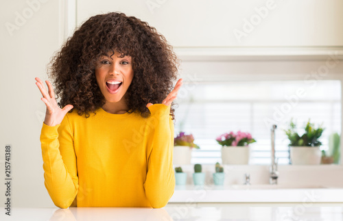 African american woman wearing yellow sweater at kitchen celebrating crazy and amazed for success with arms raised and open eyes screaming excited. Winner concept